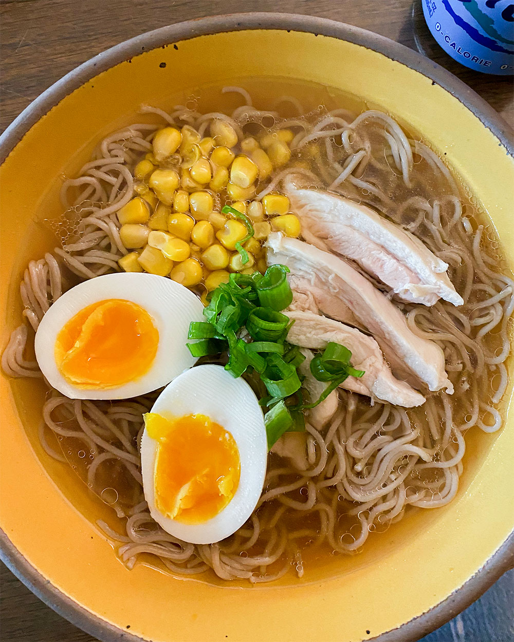 a bowl of ramen with an egg, corn, and scallions